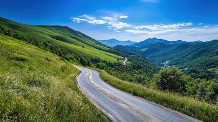 Fototapeta premium A winding road through lush green hills under a clear blue sky in a mountainous region during the daytime