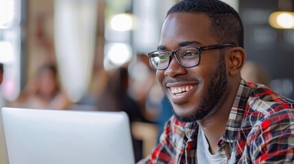 Obraz premium A man wearing glasses is smiling and looking at a laptop