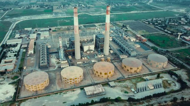 Aerial view of pipes of thermal power plant. City thermal power station among urban areas, top view. Aerial cinematic position gas turbine plant station. Tall Chimneys in Muzaffargarh, Multan Pakistan