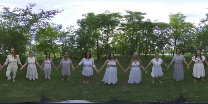 This 360-degree video features 11 women wearing white dresses, dancing in a circle in a forest. The women are all barefoot and have long, flowing hair. They are dancing in a clockwise direction, and
