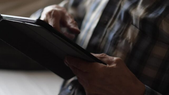 pensioner actively uses gadget tablet computer in everyday life while at home, elderly person hands scroll news feed on gadget screen