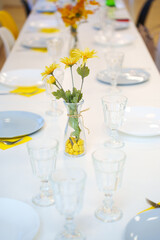 A served table with a white tablecloth, empty dishes and yellow flowers in vases. Beautiful serving and serving of dishes at the banquet. Catering.