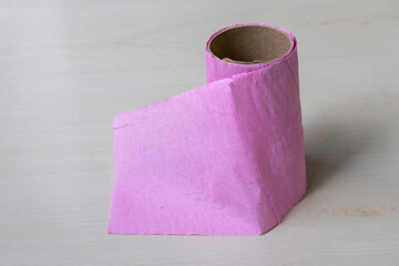 Pink toilet tissue paper, almost at its end, is placed on a wooden surface.