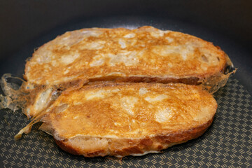 Two pieces of toast are in a pan, one of which is slightly burnt