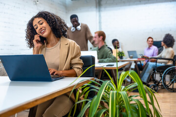 Woman talking to mobile and using laptop in a coworking