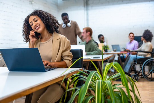 Woman talking to mobile and using laptop in a coworking