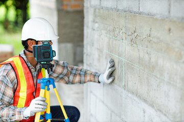 Obraz premium Construction worker is using cross-line laser level meter with line green beam to mark the floor in construction site. Tools for measuring distances.