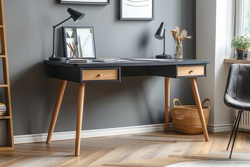 Scandinavian style desk with black top and light wood legs, featuring two drawers in an office setting with gray walls and modern metal elements.
