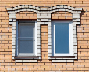 Two windows with white frames sit on a brick wall