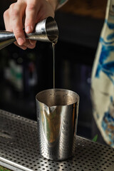 Bartender pouring liquid from a jigger into a shaker
