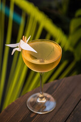A cocktail in a coupe glass served straight up, garnished with a paper origami bird