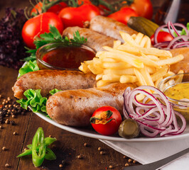 Delicious grilled sausages served with french fries and dipping sauces on rustic wooden table