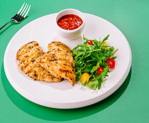 Grilled chicken breast on white plate with arugula and tomato salad