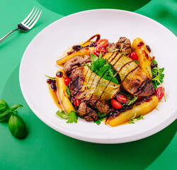 Gourmet salad with chicken liver, baked pear, tomatoes and arugula being served on white plate