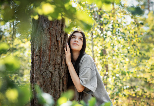 Young woman enjoying a peaceful moment by a tree in a lush green forest during daylight