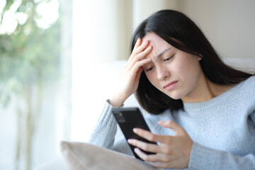 Fototapeta premium Worried asian woman checking smart phone at home