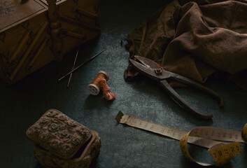 Still life composed from tailor's old tools and accessories such as scissors, measuring tape, leather fabric, sewing box in scene. Sewing supplies in dark and moody vintage style