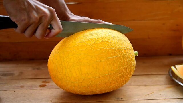 The man use knife split the orange melon on wood plate