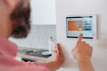 Man using smart thermostat, adjusting, lowering heating temperature at home. Concept of...