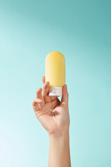 A yellow lotion bottle is held by a model hand-held device against a blue background. The product's is highlighted by the contrasting colors, which work well with the commercial image sample.
