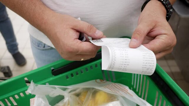 Buyer checking a receipt for paying for groceries in a store near the cash register against the backdrop of a grocery cart. Shopping at the supermarket. Product prices.