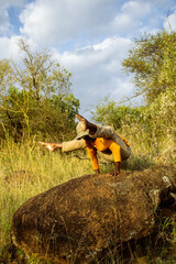 A young black woman practising yoga and meditation outdoors on a rock in the countryside