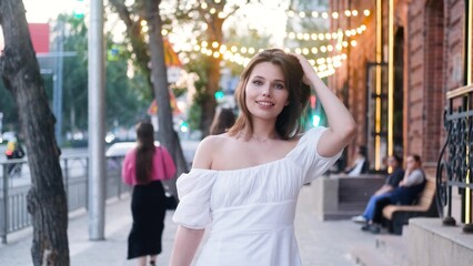 Portrait of a beautiful young woman in a cute white dress on a city street in the evening