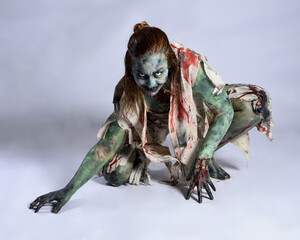 portrait of scary female model wearing spooky halloween costume, ripped clothes and fake blood like an undead demon apocalyptic zombie character. Isolated figure, crawling poses dark studio background