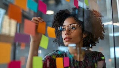 Woman with curly hair and glasses looking at sticky notes on a glass wall