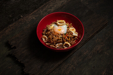 Stir Fried rice Pork and squid with Holy Basil and Chilies and egg yolk in red plate on old wooden table