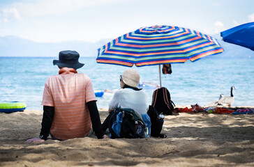 Couple sitting on the sandy Pope Beach.  Unrecognizable people playing in the water. South Lake Tahoe.