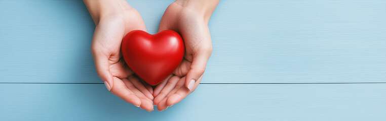 Fototapeta premium Love and Care in Hands: Conceptual Image of Holding a Red Heart on Light Blue Background with Copy Space for Web Banner Design