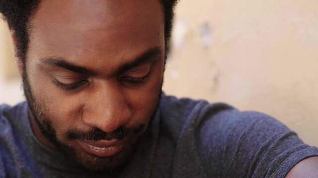 A young black man looks directly at the camera, appearing very sad and on the verge of tears, expressing deep emotional turmoil.