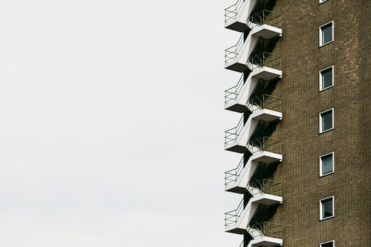 Close-up of a residential building's side, showcasing a pattern of balconies against a minimalist sky, highlighting urban life and modern architectural design.