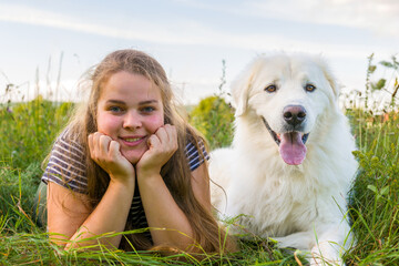 Beautiful young woman and her cute large white Great Pyrenees dog laying in tall grass meadow, enjoying time together. Pet owner, pet love, dog frienship concept.