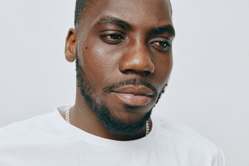 Portrait of a thoughtful young man with a serious expression, wearing a plain white t shirt and a...