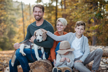 Fototapeta premium Portrait of family sitting in the middle autumn forest. Nuclear family with dog spending weekend outdoors.
