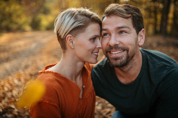Fototapeta premium Couple in love on a walk in autumn forest. Husband and wife standing in the middle of forest, touching with foreheads.