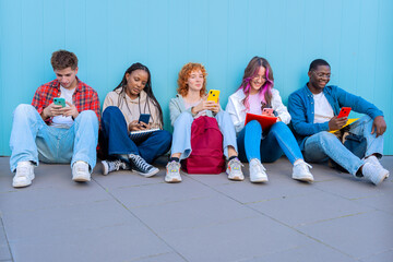 A diverse group of five smiling young students sit together on the floor, smiling and interacting on their smartphones against a blue background.