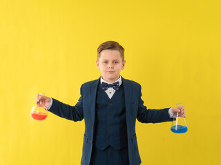 a school-age boy in a jacket holds glass flasks with reagents, a chemistry lesson