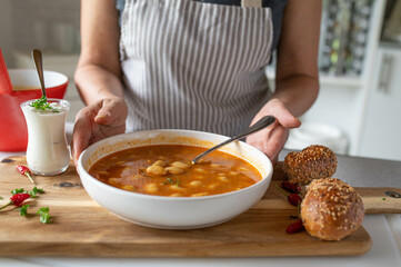Woman with apron serving a delicious homemade vegan white bean soup on kitchen counter