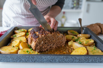 Fresh and homemade cooked meatloaf with potatoes prepared by a woman with apron in the kitchen