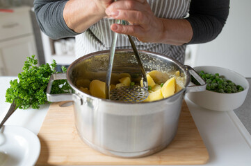 Woman mashing potatoes with a potato masher in the kitchen