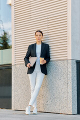 European woman in black jacket standing near office wall waiting for interview time