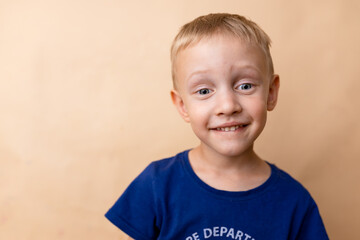 Fototapeta premium Smiling young boy in a blue shirt against a plain background, showcasing joy and innocence in a playful pose