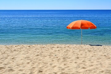 Serene beach scene with single orange umbrella clear blue sky