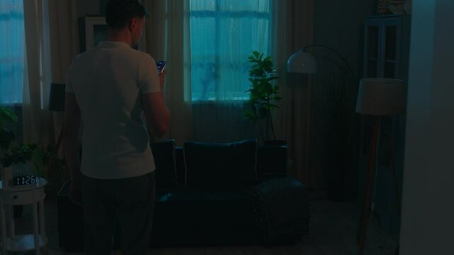 Smart home system man walking in dark room distant control electricity modern futuristic house apartment Wi-Fi managing lightness night guy male homeowner use mobile phone turn light on smartphone app