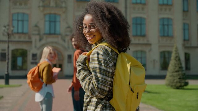 Three multiracial student friends African American guy male man Caucasian women females girls walking going outdoors outside of college academy university high school back view turn around smiling