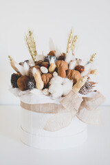 Beautiful handmade Christmas bouquet of nuts, pinecones and cotton flowers in round gift box against white background. Holiday floral decor.