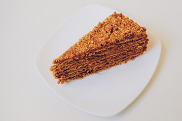 Slice of delicious homemade Medovik or Russian Honey Cake on white background. Layer sponge cake with baked condensed milk covered with crumbs. Popular dessert in countries of the former Soviet Union.